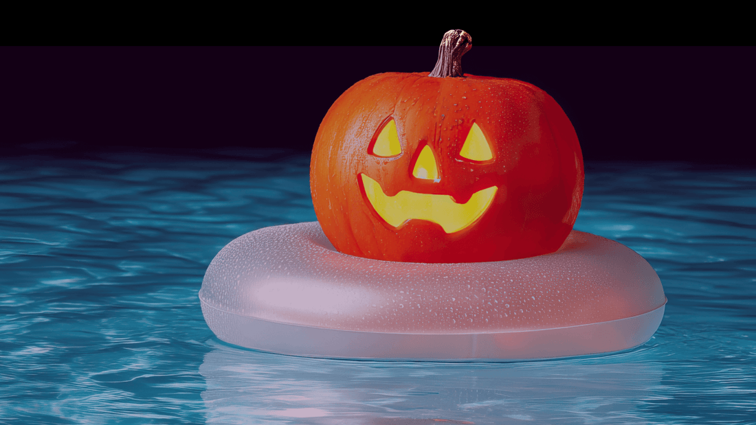 A carved, smiling jack-o'-lantern floats in a swimming pool on a white inflatable ring.