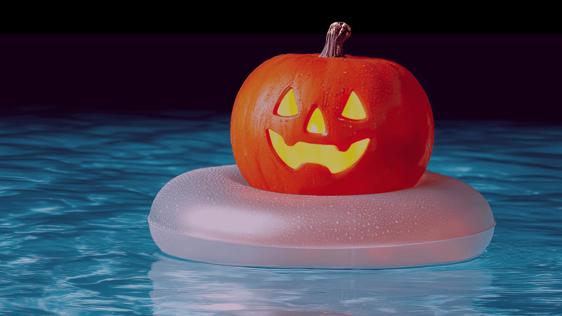 A carved, smiling jack-o'-lantern floats in a swimming pool on a white inflatable ring.