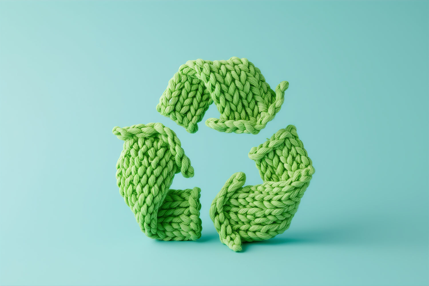 Green knitted recycling symbol on a light blue background