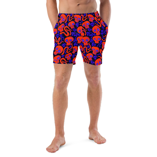 Person wearing Halloween themed organic swim trunks with a skulls and snakes pattern on a white background