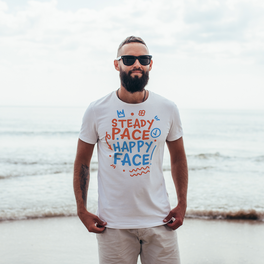 Man wearing a white organic swim shirt with colorful text on a beach