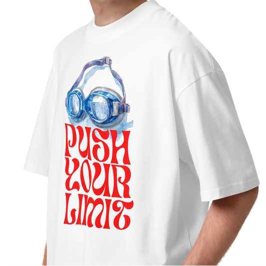 A young man wearing a white short-sleeve crewneck organic oversized t-shirt by Lane Line Threads featuring a graphic print of blue swim goggles above the text 'PUSH YOUR LIMIT' in a bold red retro font.