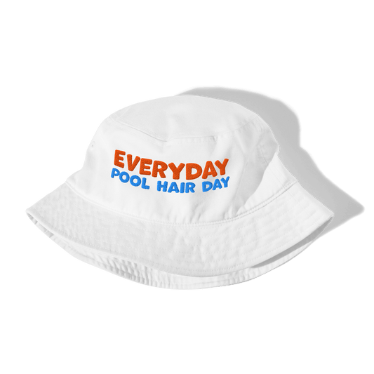 White folded organic cotton bucket hat with "EVERYDAY" in orange and "POOL HAIR DAY" in blue embroidered text. Eco-friendly, breathable, and biodegradable swimmer hat.