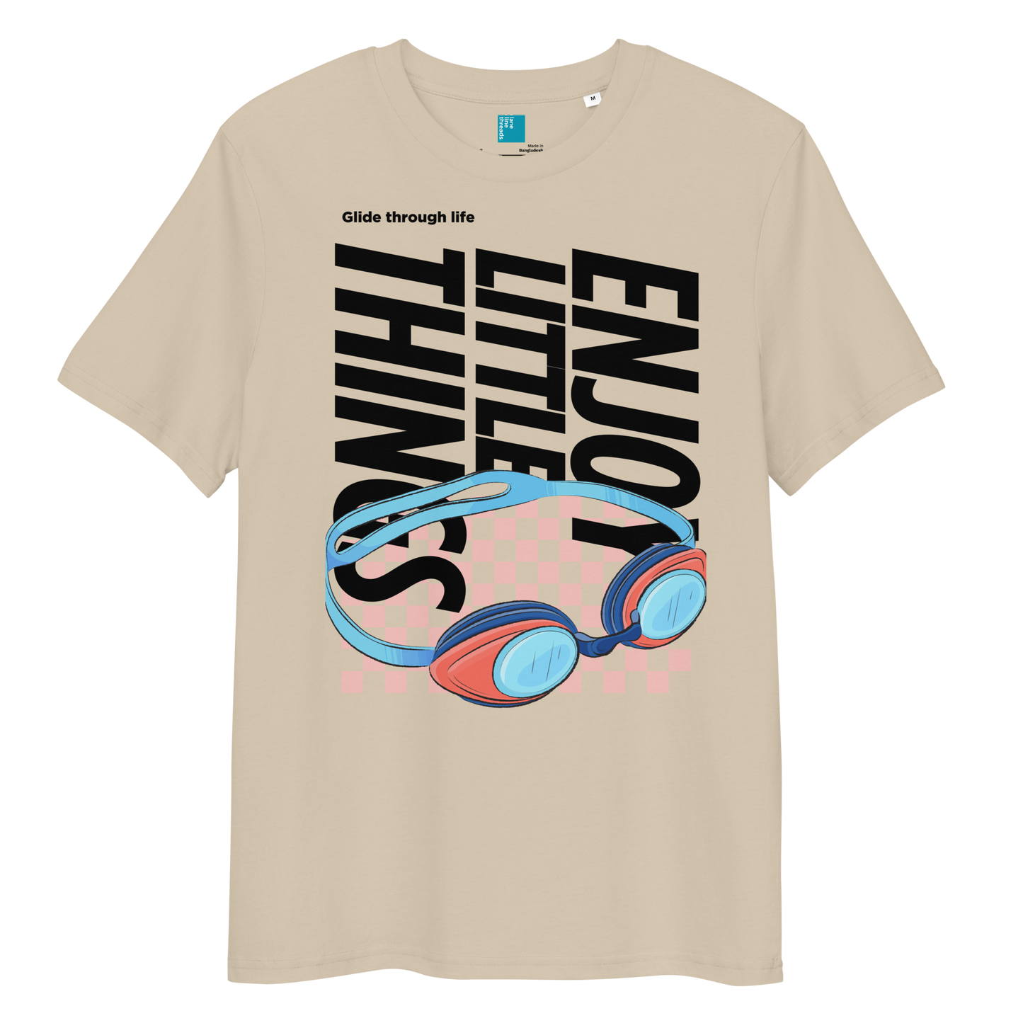Desert dust eco-friendly t-shirt featuring vibrant blue and red swimming goggles with a checkered background, and bold black text "ENJOY THE LITTLE THINGS" rotated vertically. Above the goggles, "Glide through life" is in smaller text. Made from 100% organic cotton, this breathable and biodegradable shirt is perfect for competitive swimmers who value comfort, performance, and sustainability. Ideal gift for swim meets or lane-protecting athletes with a sense of humor.