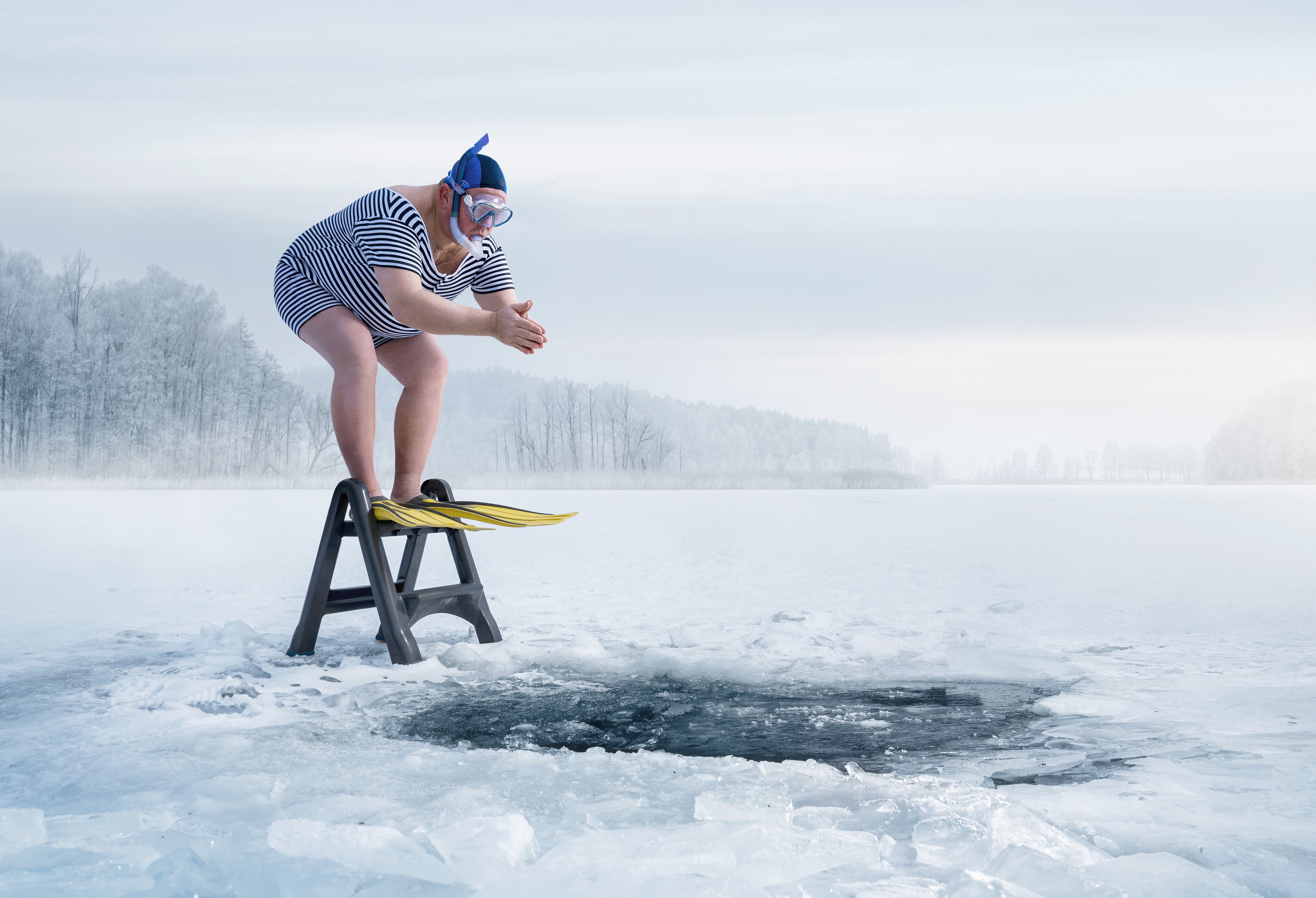 Person in a swimsuit and goggles standing on a small platform over a hole in a frozen lake.