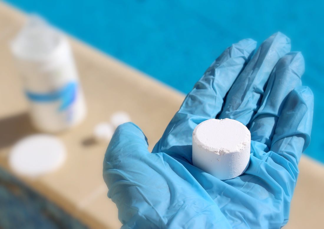 Blue-gloved hand holding a white chlorine tablet with a blurred background