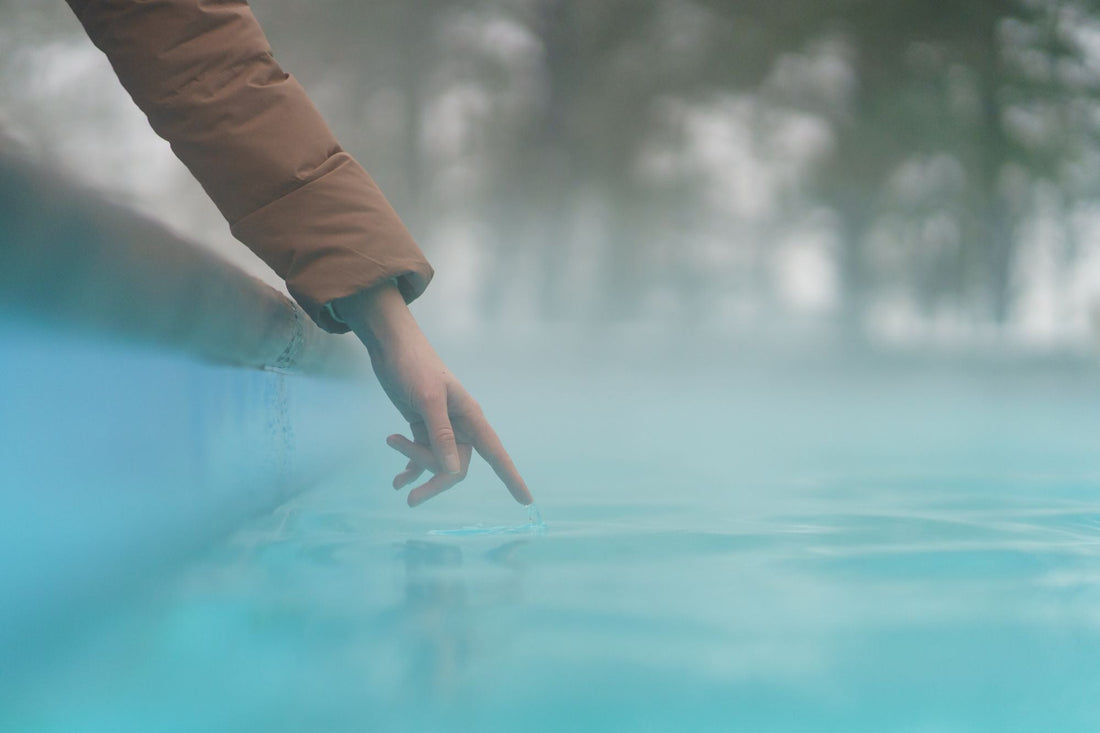 Hand reaching into a pool of water with a blurred background illustrated all time back to practice skincare for swimmers routine
