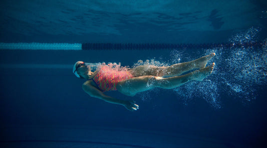 Person swimming underwater in a pool with visible swim lane lines.