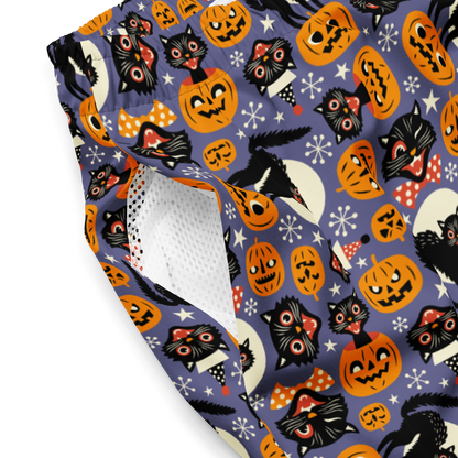 Halloween-themed recycled swim trunks with cats, pumpkins, and ghosts on a purple background close-up