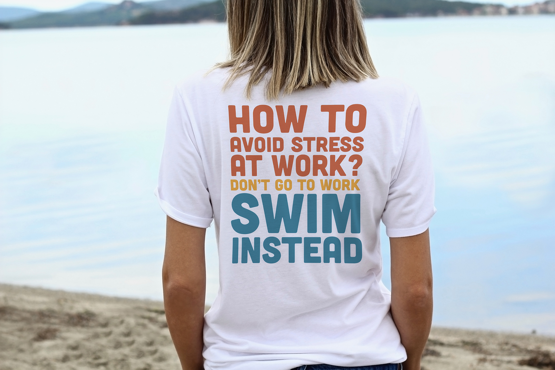Person wearing a t-shirt with humorous text about avoiding stress at work by swimming, standing on a beach.
