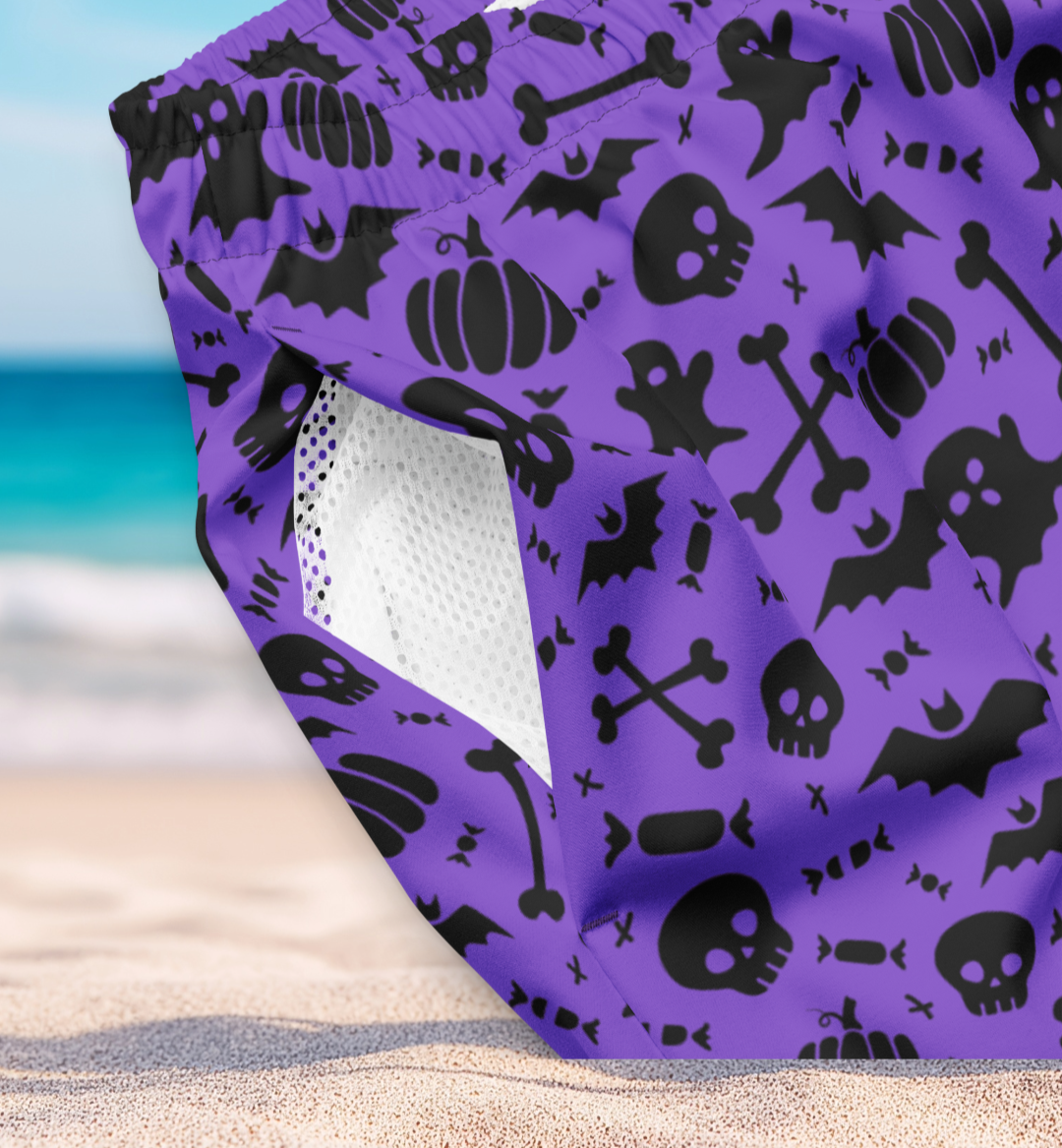 Organic purple swim trunks with black Halloween patterns on a sandy surface