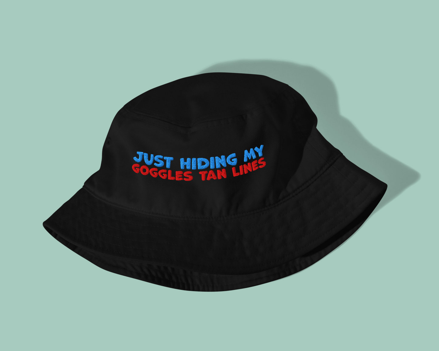 Black organic post-swim bucket hat with text 'Just hiding my goggles tan lines' on a light green background