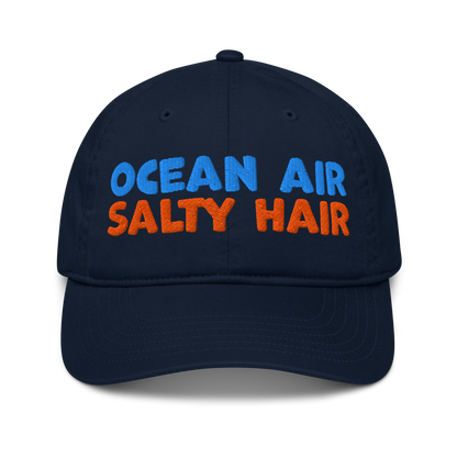 Navy organic cotton baseball cap with "OCEAN AIR" in blue and "SALTY HAIR" in orange embroidered text.