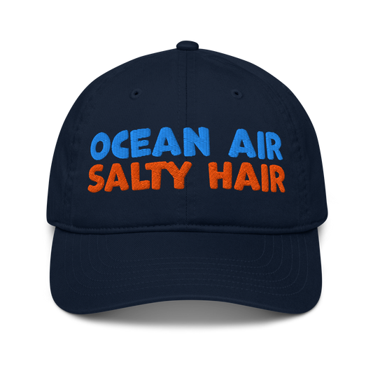 Navy organic cotton baseball cap with "OCEAN AIR" in blue and "SALTY HAIR" in orange embroidered text.