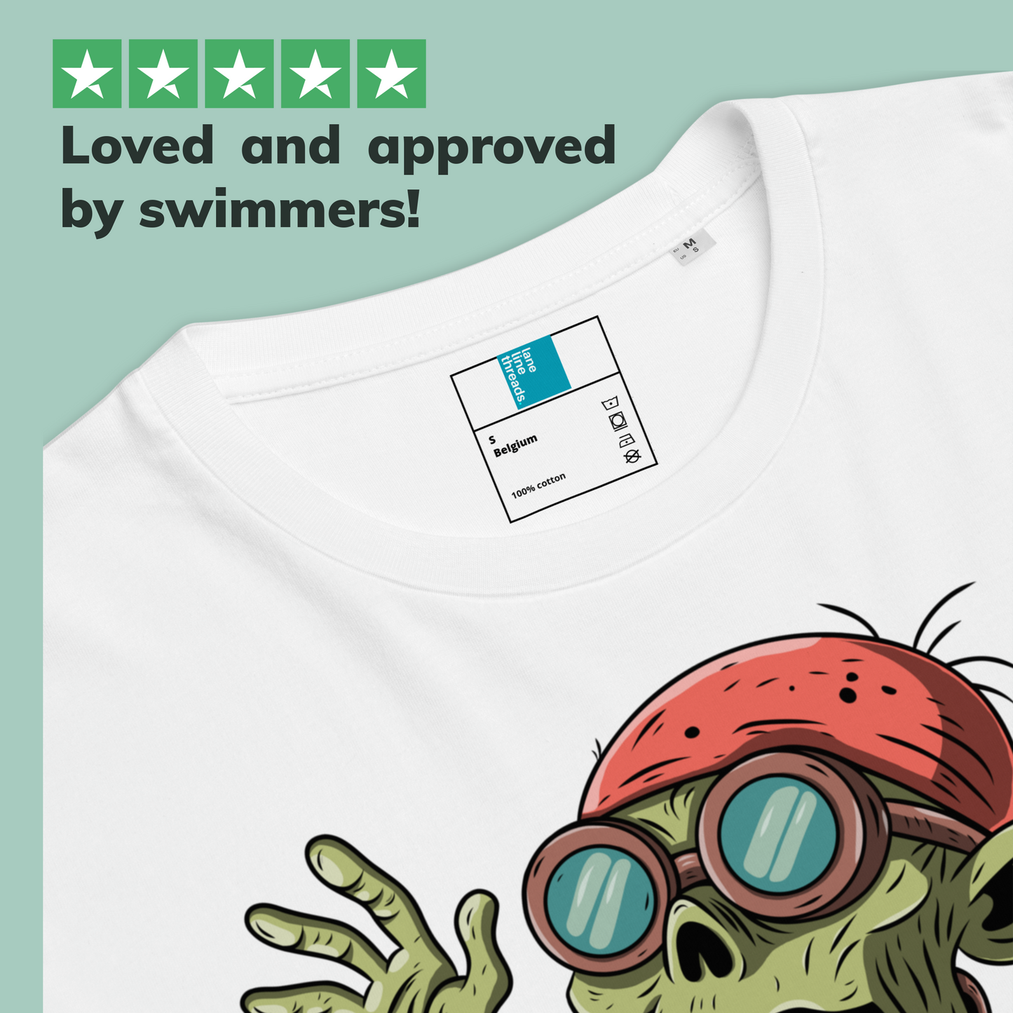 White organic Halloween swim shirt with a cartoon zombie character wearing goggles and a red cap, on a light green background with text 'Loved and approved by swimmers!'.
