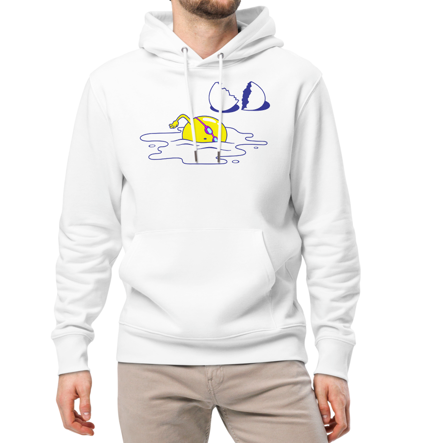 A man modeling an organic hoodie in white by Lane Line Threads featuring a graphic of a swimming yellow egg yolk with goggles and a cracked shell, paired with beige pants and white sneakers, against a plain white background.
