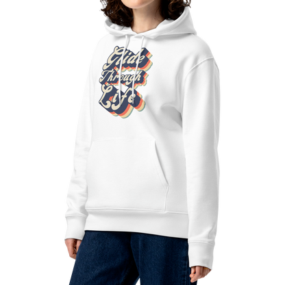 A woman with curly brown hair wearing an organic hoodie with "Glide Through Life" retro 3D typography on white GOTS and OCS certified cotton, designed for swimmer recovery, paired with dark blue jeans, set against a plain white background