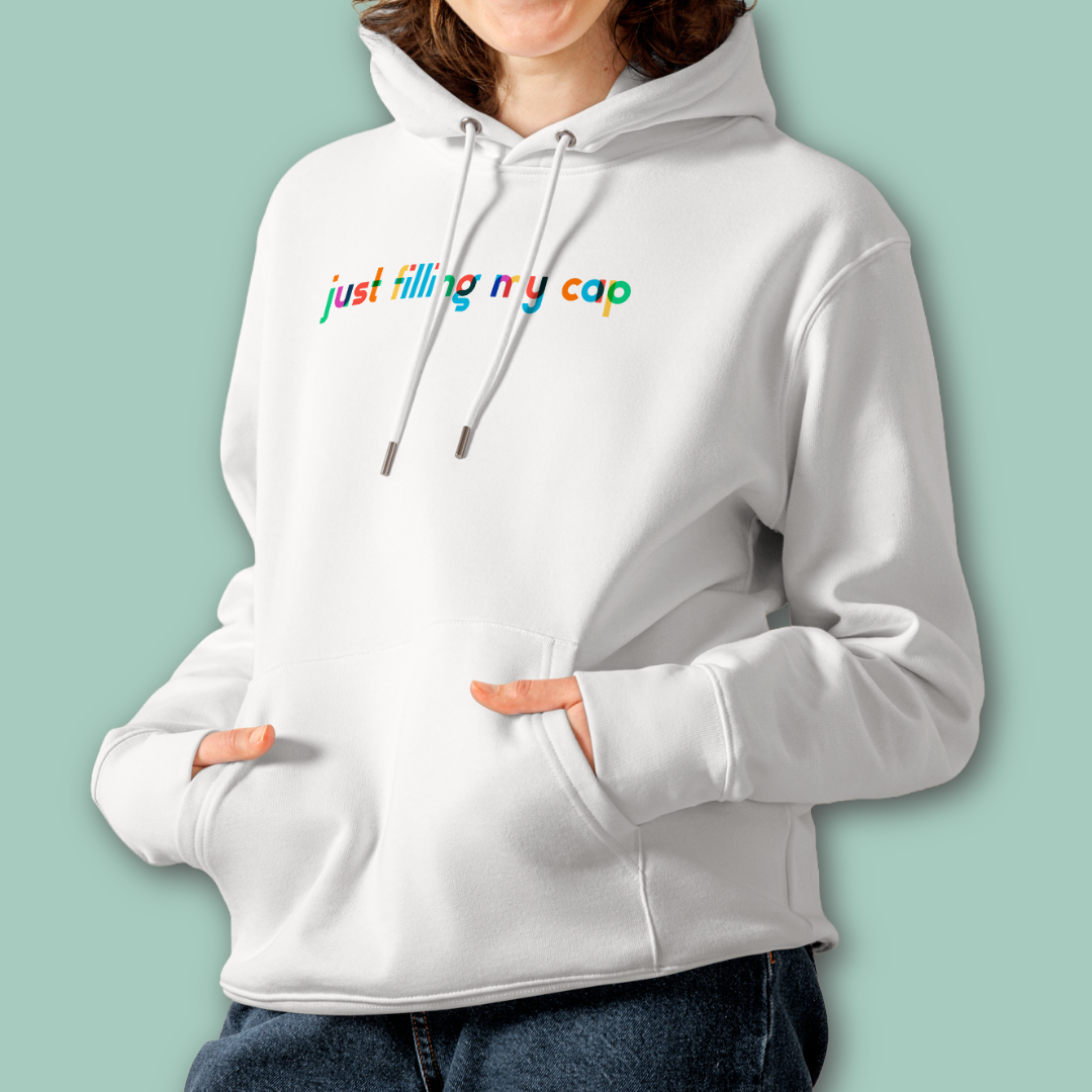 A female person wearing an organic hoodie in white by Lane Line Threads with colorful “just filling my cap” text on the chest, made from GOTS and OCS certified organic cotton.