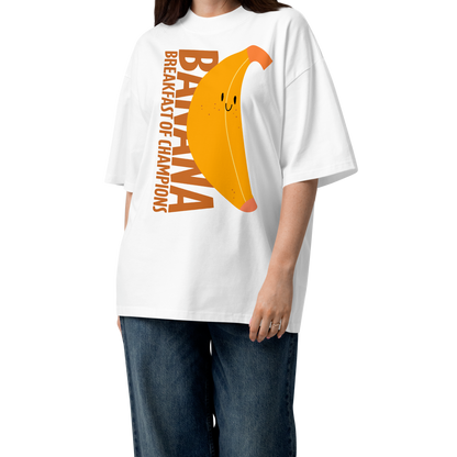 A woman modeling a white short-sleeve crewneck organic oversized t-shirt by Lane Line Threads featuring a graphic print of a smiling yellow banana with the text 'BANANA BREAKFAST OF CHAMPIONS' in brown. She is wearing wide-leg blue jeans and brown sandals against a plain white background.