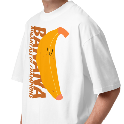 A young man with curly brown hair wearing a white short-sleeve crewneck organic oversized t-shirt by Lane Line Threads featuring a graphic print of a smiling yellow banana with the text 'BANANA BREAKFAST OF CHAMPIONS' in brown.