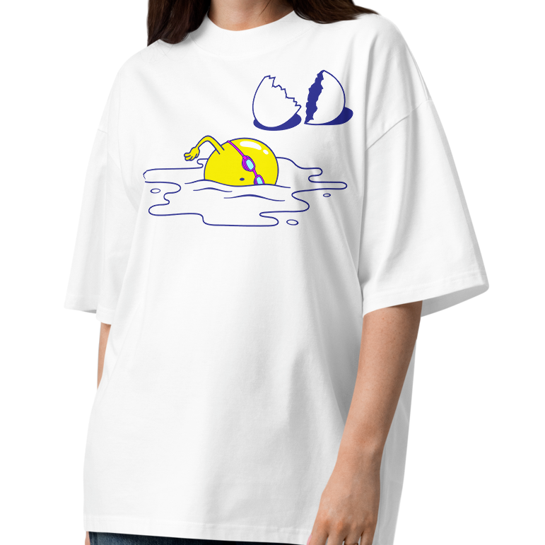 A woman modeling a white short-sleeve crewneck organic oversized t-shirt by Lane Line Threads featuring a graphic print of a yellow cartoon egg yolk swimmer character breaking an egg on a white background.