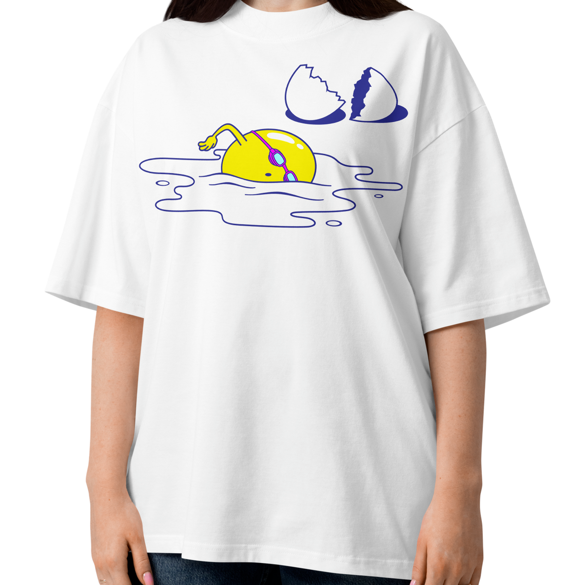 A woman modeling a white short-sleeve crewneck organic oversized t-shirt by Lane Line Threads featuring a graphic print of a yellow cartoon egg yolk swimmer character breaking an egg on a white background.