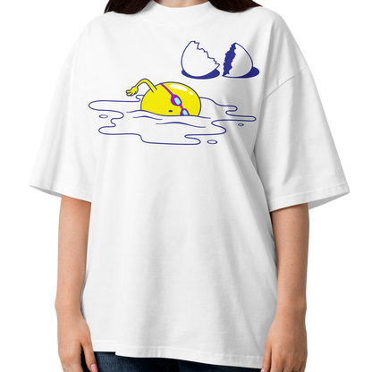 A woman modeling a white short-sleeve crewneck organic oversized t-shirt by Lane Line Threads featuring a graphic print of a yellow cartoon egg yolk swimmer character breaking an egg on a white background.