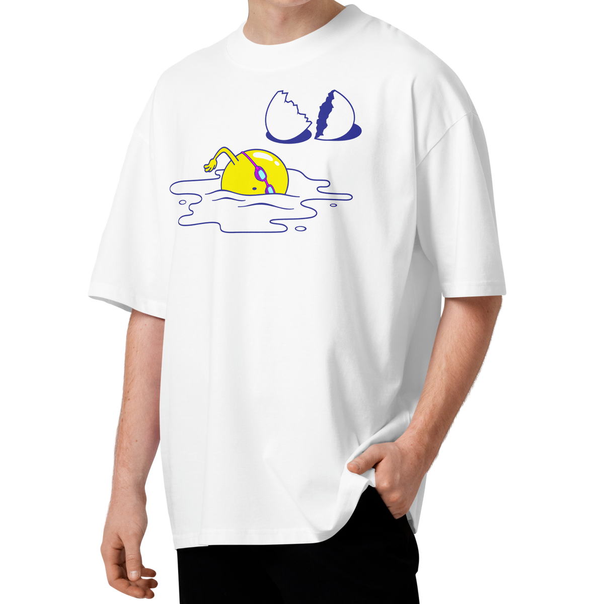 A young man with curly brown hair wearing a white short-sleeve crewneck organic oversized t-shirt by Lane Line Threads featuring a graphic print of a yellow cartoon egg yolk swimmer character breaking an egg on a white background.