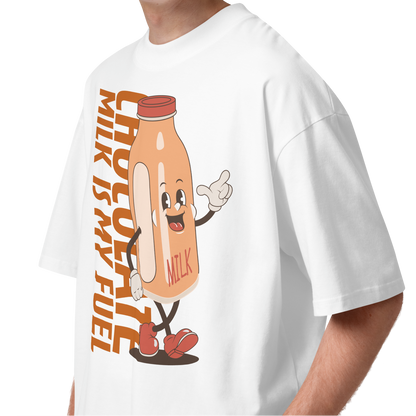 A young man with curly brown hair wearing a white short-sleeve crewneck organic oversized t-shirt by Lane Line Threads featuring a cartoon graphic of a vintage milk bottle character with the text 'CHOCOLATE MILK IS MY FUEL' printed vertically in orange and inspired by Katie Ledecky.