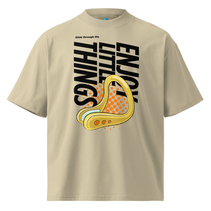 A beige short-sleeve crewneck organic oversized t-shirt by Lane Line Threads featuring a bold graphic print on the front. The design includes the text 'Enjoy Little Things' in black, a gold-colored swimming nose clip illustration, and a halftone pattern in orange.