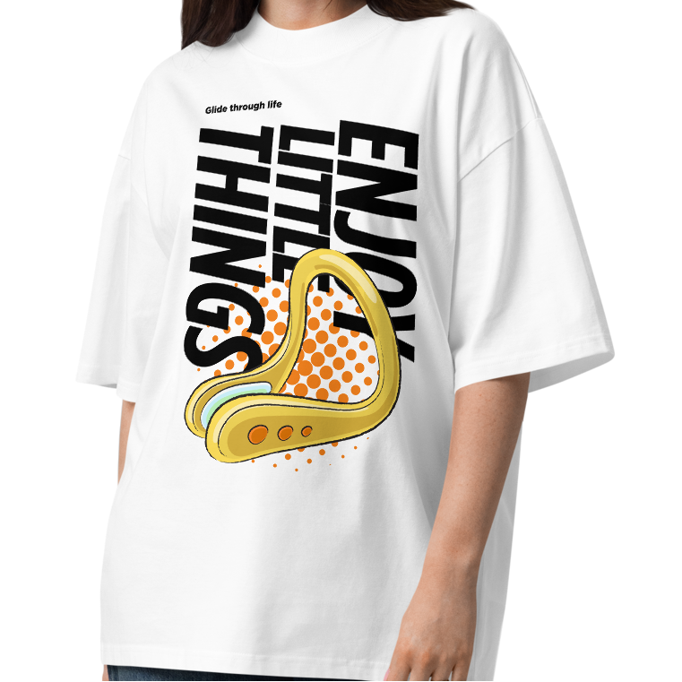 A young woman modeling a white short-sleeve crewneck organic oversized t-shirt by Lane Line Threads featuring a bold graphic print on the front. The design includes the text 'Enjoy Little Things' in black, a gold-colored swimming nose clip illustration, and a halftone pattern in orange.