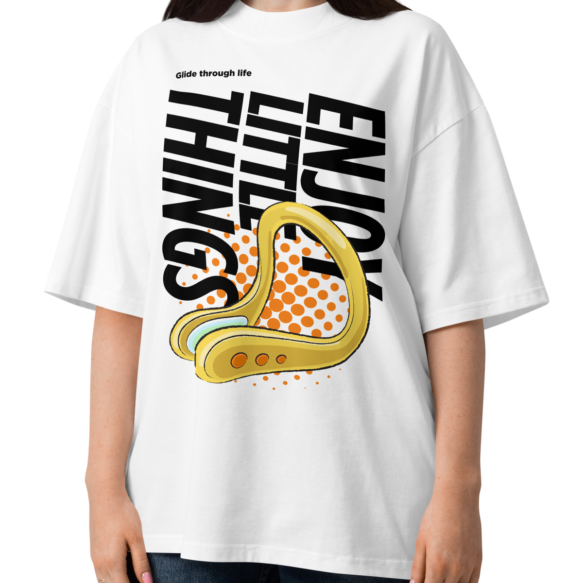 A woman modeling a white short-sleeve crewneck organic oversized t-shirt by Lane Line Threads featuring a bold graphic print on the front. The design includes the text 'Enjoy Little Things' in black, a gold-colored swimming nose clip illustration, and a halftone pattern in orange.