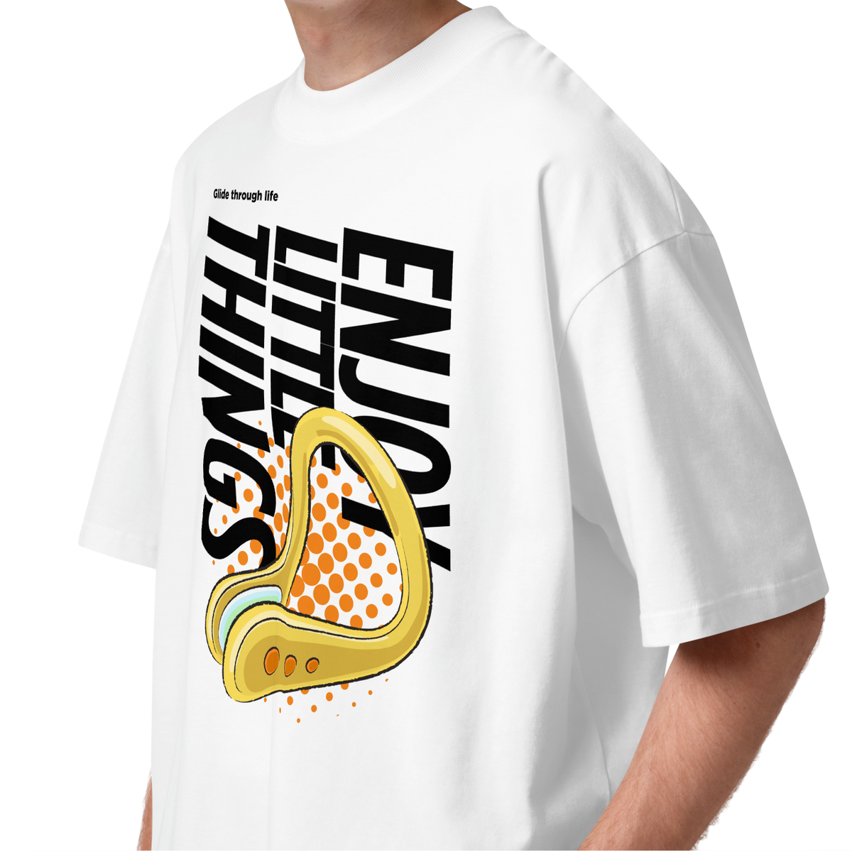 A young man wearing a white short-sleeve crewneck organic oversized t-shirt by Lane Line Threads featuring a bold graphic print on the front. The design includes the text 'Enjoy Little Things' in black, a gold-colored swimming nose clip illustration, and a halftone pattern in orange.