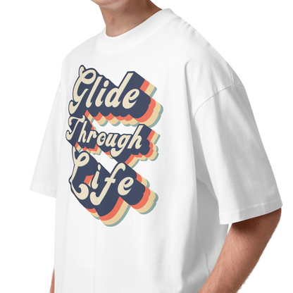 A young man with curly brown hair wearing an organic oversized t-shirt by Lane Line Threads in white with retro “Glide Through Life” layered swim graphic