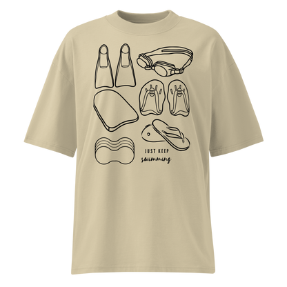 A beige short-sleeve organic oversized t-shirt by Lane Line Threads with a black line art graphic of swimming gear, including flippers, goggles, paddles, kickboard and a flip-flop, with the text 'JUST KEEP swimming' printed on the front.