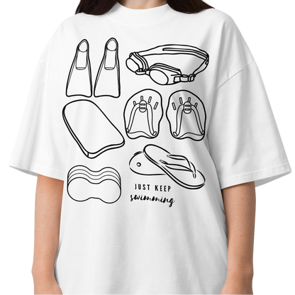 A woman wearing a short-sleeve organic oversized t-shirt by Lane Line Threads with a black line art graphic of swimming gear, including flippers, goggles, paddles, kickboard and a flip-flop, with the text 'JUST KEEP swimming' printed on the front.
