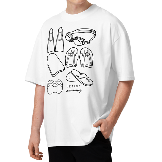 A man wearing a white organic oversized t-shirt with a black line art graphic of various swimming accessories and the text 'JUST KEEP swimming' on the front, paired with black pants, set against a plain white background.