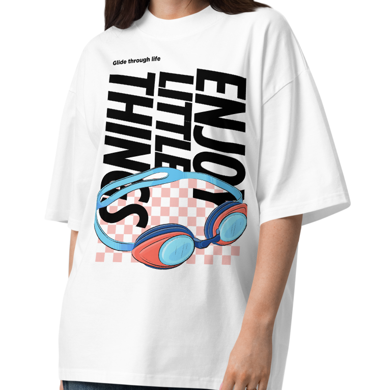 A woman modeling an organic oversized t-shirt in white with colorful swim goggles, bold “Enjoy Little Things” lettering, and “Glide Through Life” graphic by Lane Line Threads.
