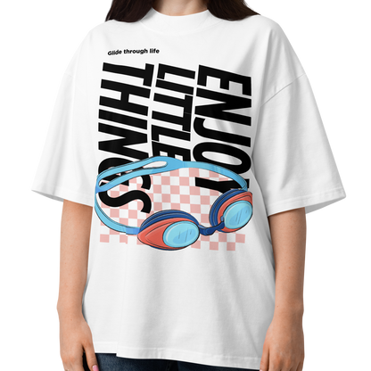 a young women wearing an organic oversized t-shirt in white with colorful swim goggles, bold “Enjoy Little Things” lettering, and “Glide Through Life” graphic by Lane Line Threads.