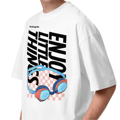 a young man wearing an organic oversized t-shirt in white with colorful swim goggles, bold “Enjoy Little Things” lettering, and “Glide Through Life” graphic by Lane Line Threads.