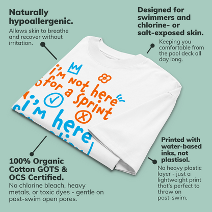 A white short-sleeve crewneck organic oversized t-shirt by Lane Line Threads with a colorful graphic print on the chest. The graphic features the text 'I'm not here for a sprint I'm here for motion!' in orange and blue handwritten-style lettering, accompanied by small doodles of a clock, a stop sign, wavy lines, and a heart. Shown on a light teal background with callout labels explaining product features and benefits.
