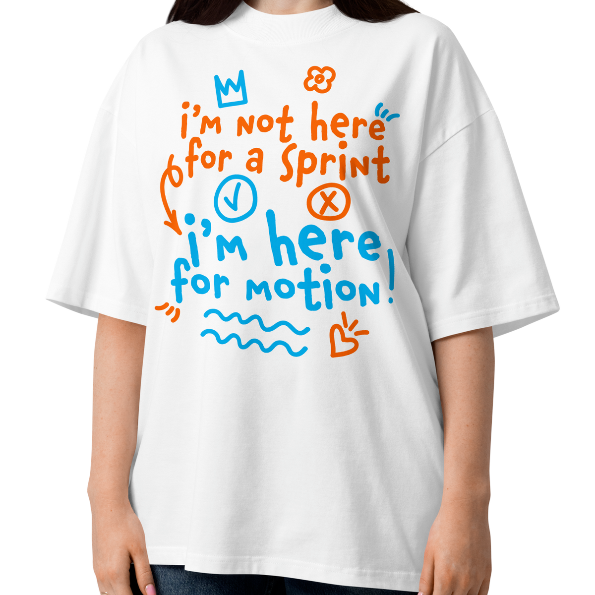 A woman wearing a white short-sleeve crewneck organic oversized t-shirt by Lane Line Threads with a colorful graphic print on the chest. The graphic features the text 'I'm not here for a sprint I'm here for motion!' in orange and blue handwritten-style lettering, accompanied by small doodles of a clock, a stop sign, wavy lines, and a heart.