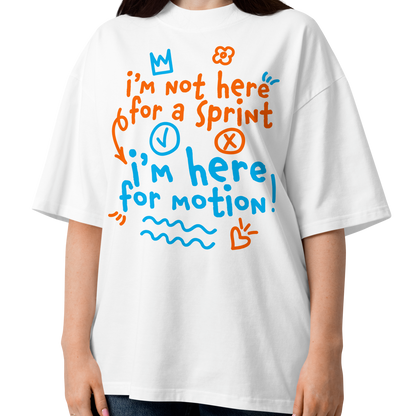 A woman wearing a white short-sleeve crewneck organic oversized t-shirt by Lane Line Threads with a colorful graphic print on the chest. The graphic features the text 'I'm not here for a sprint I'm here for motion!' in orange and blue handwritten-style lettering, accompanied by small doodles of a clock, a stop sign, wavy lines, and a heart.
