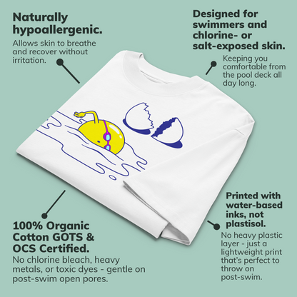 A white organic oversized t-shirt by Lane Line Threads laid folded flat on a pale green background with callout text describing its hypoallergenic, swim-friendly, and printed features. The shirt has a cartoon yellow egg yolk with blue outlines and a cracked shell graphic.
