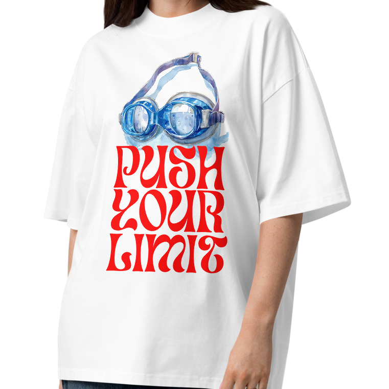 A woman modeling a white organic oversized t-shirt by Lane Line Threads with a retro graphic of swim goggles and the text 'PUSH YOUR LIMITS' in red, paired with wide-leg dark blue jeans and brown sandals, on a solid white background.