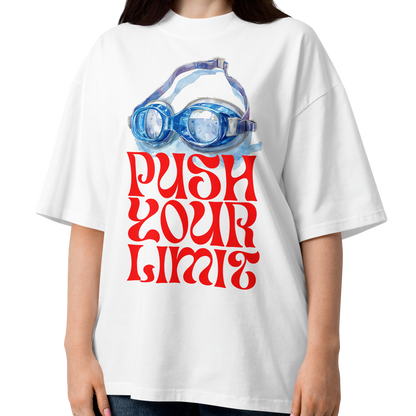 A woman wearing a white organic oversized t-shirt by Lane Line Threads with a blue swim goggles and red 'PUSH YOUR LIMIT' text design, paired with blue jeans, against a plain white background.