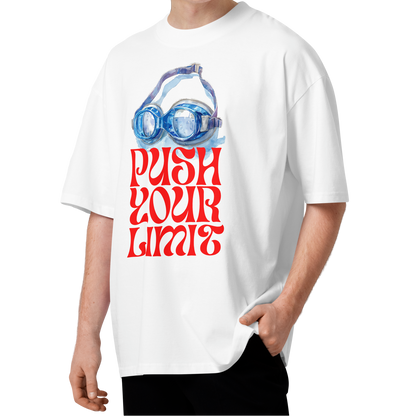 A young man wearing a white short-sleeve crewneck organic oversized t-shirt by Lane Line Threads featuring a graphic print of blue swim goggles above the text 'PUSH YOUR LIMIT' in a bold red retro font.