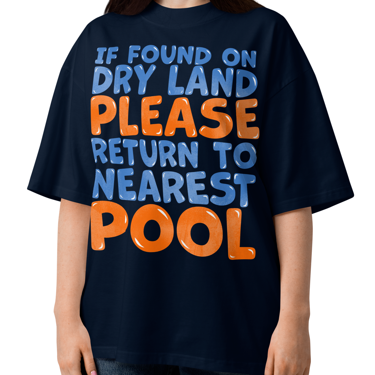 A woman modeling a navy blue organic oversized t-shirt with a bold graphic text that reads 'IF FOUND ON DRY LAND PLEASE RETURN TO NEAREST POOL' in light blue and orange lettering, set against a plain white background.