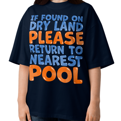 A woman modeling a navy blue organic oversized t-shirt with a bold graphic text that reads 'IF FOUND ON DRY LAND PLEASE RETURN TO NEAREST POOL' in light blue and orange lettering, set against a plain white background.