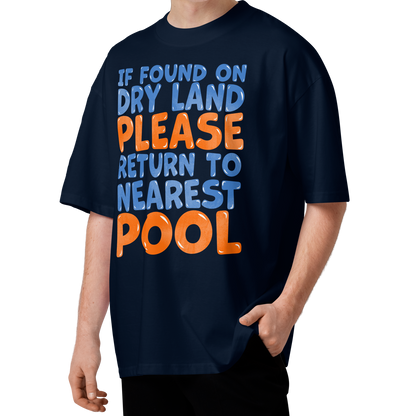 A man wearing a navy blue organic oversized t-shirt with the text 'IF FOUND ON DRY LAND PLEASE RETURN TO NEAREST POOL' in blue and orange lettering, set against a plain white background.